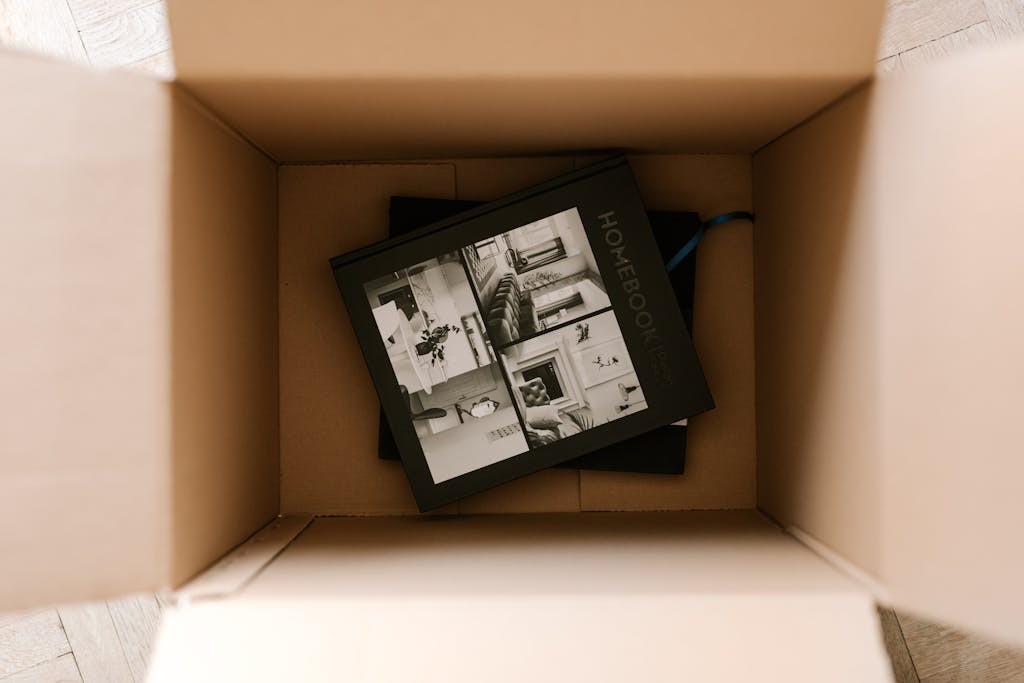Top view of an open cardboard box containing a home design book, in natural daylight.